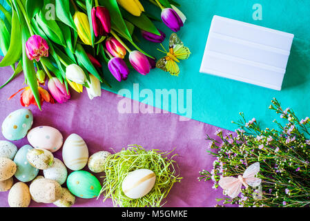 Frohe Ostern Frühling Schuß von oben als flatlay mit leeren Leuchtkasten für Meldung und bunte Tulpen, Blumen und Ostereier Stockfoto