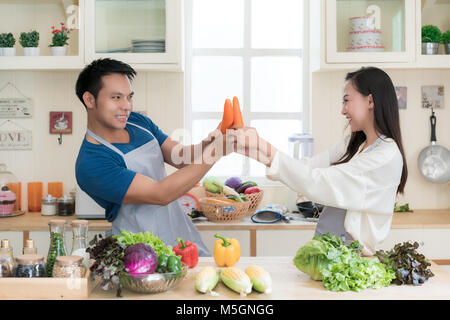 Spaß asiatischen Paar mock kämpft mit Karotten als Asiatische paar Kochen gesunde Mahlzeit zusammen mit frischem Gemüse und Kräutern. Stockfoto