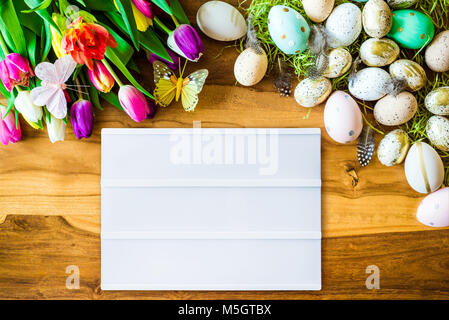 Frohe Ostern Frühling Schuß von oben als flatlay mit leeren Lightbox für Meldung und bunte Tulpen und Ostereier auf Holz- Hintergrund Stockfoto