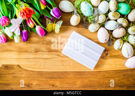 Frohe Ostern Frühling Schuß von oben als flatlay mit leeren Lightbox für Meldung und bunte Tulpen und Ostereier auf Holz- Hintergrund Stockfoto