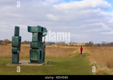 Snape Maltings, Suffolk. 23 Feb, 2018. UK Wetter: hellen, sonnigen Nachmittag an Snape Maltings, Suffolk. Die Familie der Mann Skulptur beobachtet ein Besucher in einem roten Mantel. Stockfoto