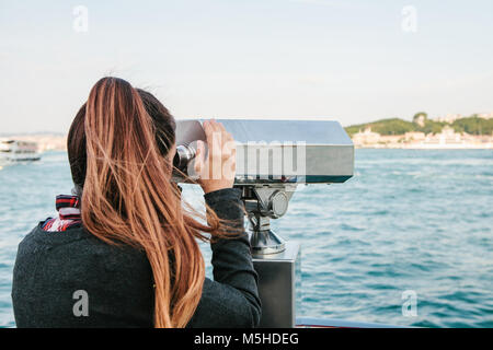 Brunette Mädchen mit Blick auf das Meer durch touristische Teleskop. Stockfoto