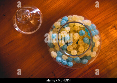 Glas Glas mit rund frosty Gelb und Blau candy auf hölzernen Tisch geöffnet Stockfoto