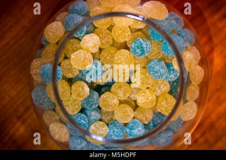 Glas Glas mit rund frosty Gelb und Blau candy auf hölzernen Tisch geöffnet Stockfoto