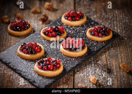 Törtchen mit frischen roten Beeren auf schwarzem Schiefer Stockfoto