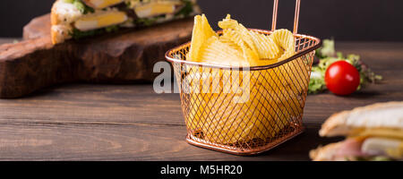 Knusprige Kartoffelchips in Kupfer Warenkorb auf alten hölzernen Hintergrund serviert mit Club Sandwich. Gesundes fast food Konzept mit kopieren. Banner. Stockfoto