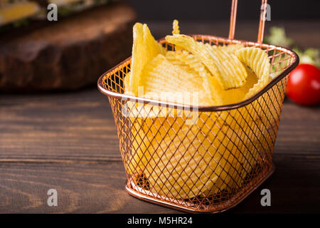 Knusprige Kartoffelchips in Kupfer Warenkorb auf alten hölzernen Hintergrund serviert mit Club Sandwich. Gesundes fast food Konzept mit kopieren. Stockfoto