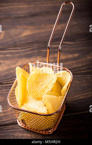 Knusprige Kartoffelchips in Kupfer Warenkorb auf alten hölzernen Hintergrund. Gesundes fast food Konzept mit kopieren. Stockfoto