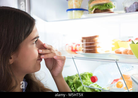 Nahaufnahme einer jungen Frau, die ihre Nase in der Nähe von Foul Essen im Kühlschrank Stockfoto