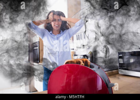 Frustrierte junge Frau bei Burnt Toast aus der Toaster in der Küche Stockfoto