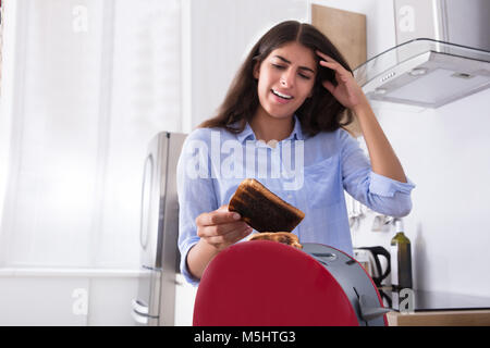 Unglückliche junge Frau mit Toast in der Küche verbrannt Stockfoto