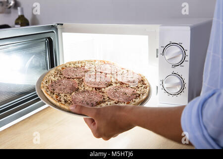 Nahaufnahme der Hand Backen Salami einer Person Pizza in der Mikrowelle Stockfoto