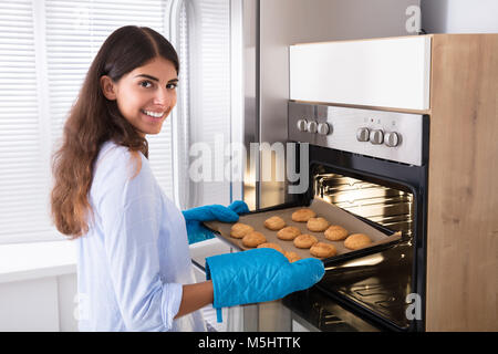 Porträt eines lächelnden Frau nehmen Sie Fach der gebackenen Plätzchen aus dem Ofen Stockfoto