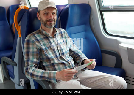 Reifer Mann holding Tickets in einem pendlerzug Stockfoto