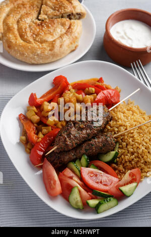 Türkische Abendessen mit Kebabs, Bulgur, geschmortem Gemüse und frische Tomaten- und Gurkensalat Stockfoto