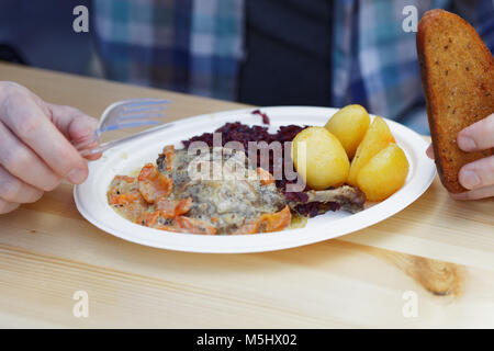 Mann essen Gebratene Entenkeule mit gedünstetem Rotkohl, gekochte Kartoffel, Karotte unter weißen Sauce in einem Street Food Restaurant Stockfoto