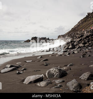 Salinas de Fuencaliente, La Palma. Kanarische Inseln Spanien. Wellen auf die Lava Beach. Einige große Lavagestein im Vordergrund für Interesse. Dieses kleine Fuencaliente de La Palma Bay ist typisch für die dramatische Küstenlinie der Insel. Die lavafelsen steigen stark an eine Felswand zu bilden. Die Sonne scheint hell die Sea Foam sehr weiß und der Himmel Hellblau. Die großen lavafelsen im Vordergrund durch das Meer, das die Härte der Meeresumwelt erodiert. Schließlich das Meer die größeren Felsen in feinen lavasand wie der Rest der Strand erodieren. Mit einer Ricoh GRII fotografiert. Stockfoto