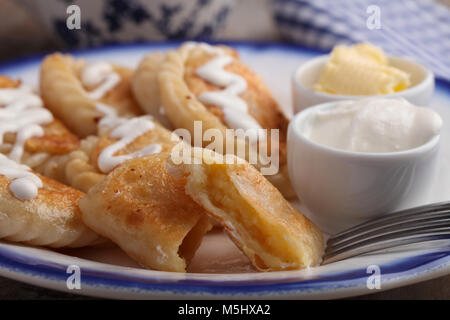 Traditionelle polnische Knödel Pierogi ruskie mit Kartoffeln, saure Sahne und Butter auf einem rustikalen Tisch Stockfoto