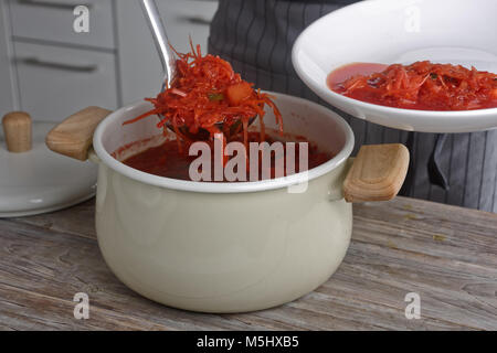 Cook Gießen der Teil der Borscht, die Suppe mit Rote Bete, Kartoffeln, Kohl, Tomaten und Zwiebel aus einem kochenden Topf in eine Schüssel Stockfoto