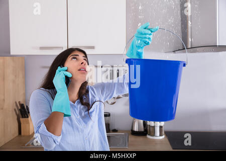 Frau Aufruf Klempner beim Sammeln von Wasser von der Decke mit Schaufel Stockfoto