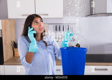 Frau Aufruf Klempner beim Sammeln von Wasser von der Decke mit Schaufel Stockfoto