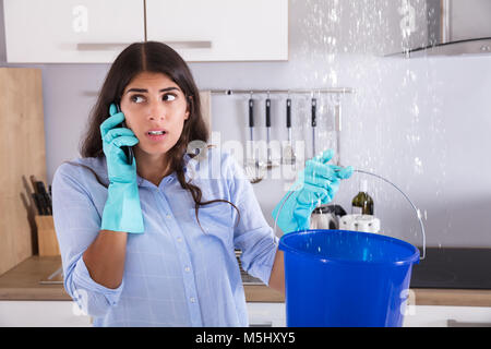 Frau Aufruf Klempner beim Sammeln von Wasser von der Decke mit Schaufel Stockfoto