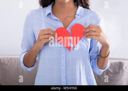 Junge Frau mit Gebrochener roter Valentine Herz aus Papier zu Hause Stockfoto