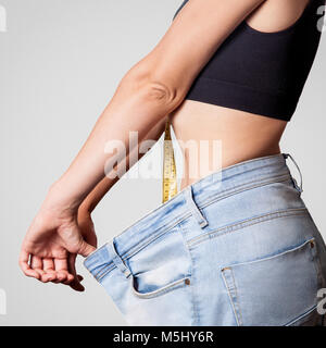 Nahaufnahme der schlanke Taille der jungen Frau in big Jeans zeigen erfolgreiche Gewichtsabnahme, isoliert auf hellgrauen Hintergrund, Diät Konzept. Stockfoto