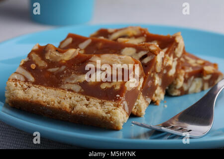 Scheiben von Karamell und Muttern Kuchen auf einem blauen Platte Stockfoto