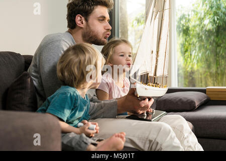 Vater und Kinder Blasen in die Segel der Toy model ship auf der Couch zu Hause Stockfoto