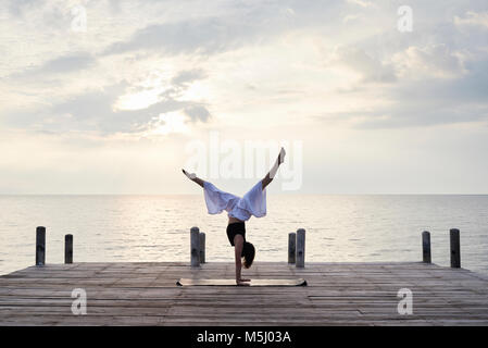 Yoga Instructor auf dem Kopf stehend auf Händen, während Yoga gegen den Sonnenuntergang und das Meer. Kep, Kambodscha. Stockfoto