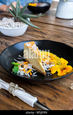 Dekoriert Käsekuchen Stück mit Blumen auf hölzernen Tisch Stockfoto