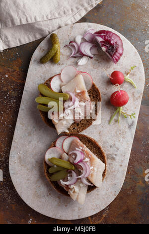 Sandwiches mit Hering, eingelegte Gurken, Rettich und Zwiebeln auf einem Marmor Schneidebrett Stockfoto