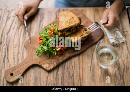 Hände, die Messer und Gabel an den hölzernen Tisch dekoriert mit Salat und knusprigem Brot Stockfoto