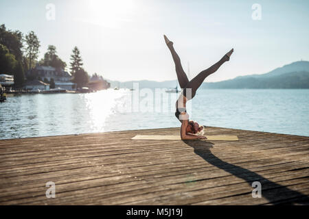 Frau praktizieren Yoga auf Steg am See Stockfoto