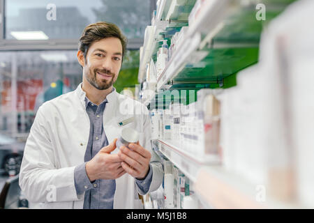 Portrait von lächelnden Apotheker mit Sahne jar am Regal in der Apotheke Stockfoto