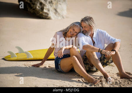 Herzlichen senior Paar mit Surfbrett liegend am Strand Stockfoto