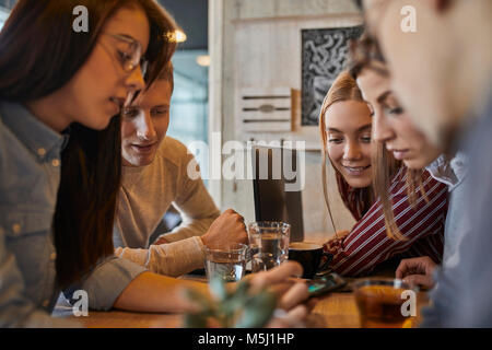 Gruppe von Freunden sind, die zusammen in einem Cafe sitzen Teilen smartphone Stockfoto