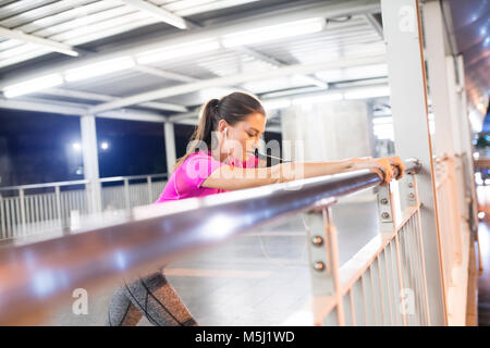 Junge Frau in Rosa sportshirt Dehnen in modernen U-Bahnhof bei Nacht Stockfoto