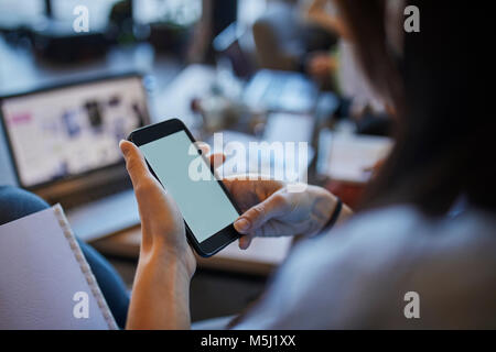 Junge Frau im Cafe mit Smartphone mit Laptop im Hintergrund Stockfoto