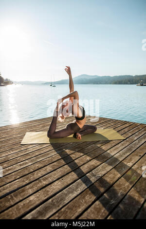 Frau praktizieren Yoga auf Steg am See Stockfoto