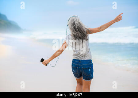Ältere Frau mit Kopfhörer tanzen am Strand Stockfoto