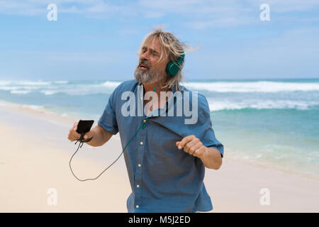 Gut aussehender älterer Mann mit Kopfhörer tanzen am Strand Stockfoto