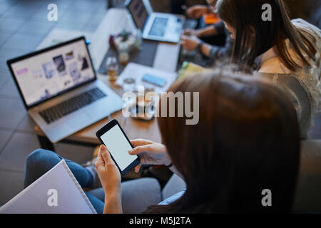 Junge Frau im Cafe Smartphone mit mit Freunden mit Laptop im Hintergrund Stockfoto