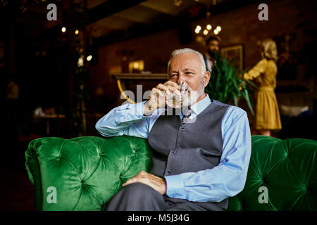 Portrait von eleganten älterer Mann sitzt auf der Couch in einer Bar trinken aus Zuhaltung Stockfoto