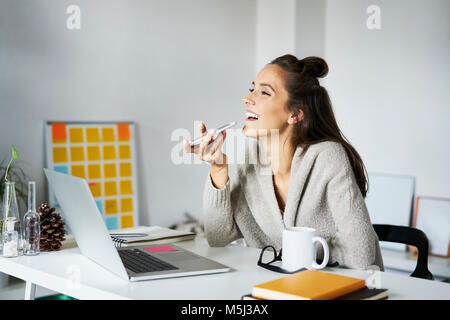 Glückliche junge Frau, die am Schreibtisch smartphone Stockfoto