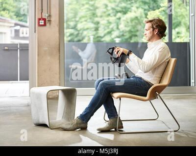Mann mit VR-Brille sitzen auf Stuhl Stockfoto