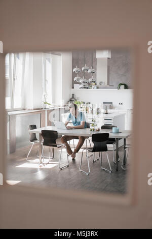 Mann am Tisch in der Küche arbeiten am Laptop Stockfoto