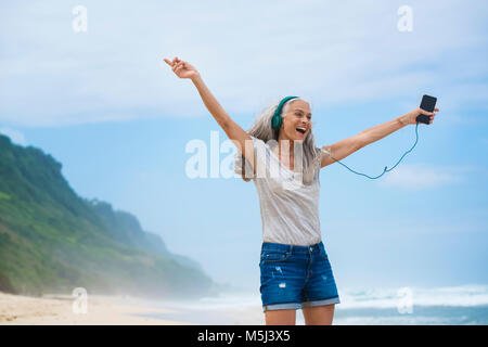Ältere Frau mit Kopfhörer tanzen am Strand Stockfoto