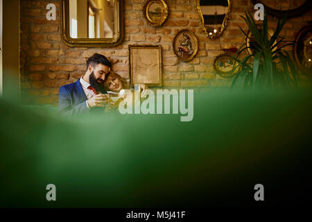 Elegantes Paar mit Getränken sitzen auf der Couch umarmt Stockfoto